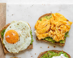 A plate with a slice of toasted whole wheat bread topped with mashed avocado, sliced boiled eggs, and a sprinkle of salt and pepper. The breakfast is served on a wooden table with a Wicoser logo in the corner.